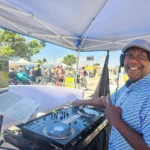 DJ SouthLAnd smiling behind his controller at an outdoor community event.