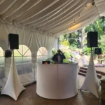 White DJ booth and coordinated speakers in a draped outdoor event tent.