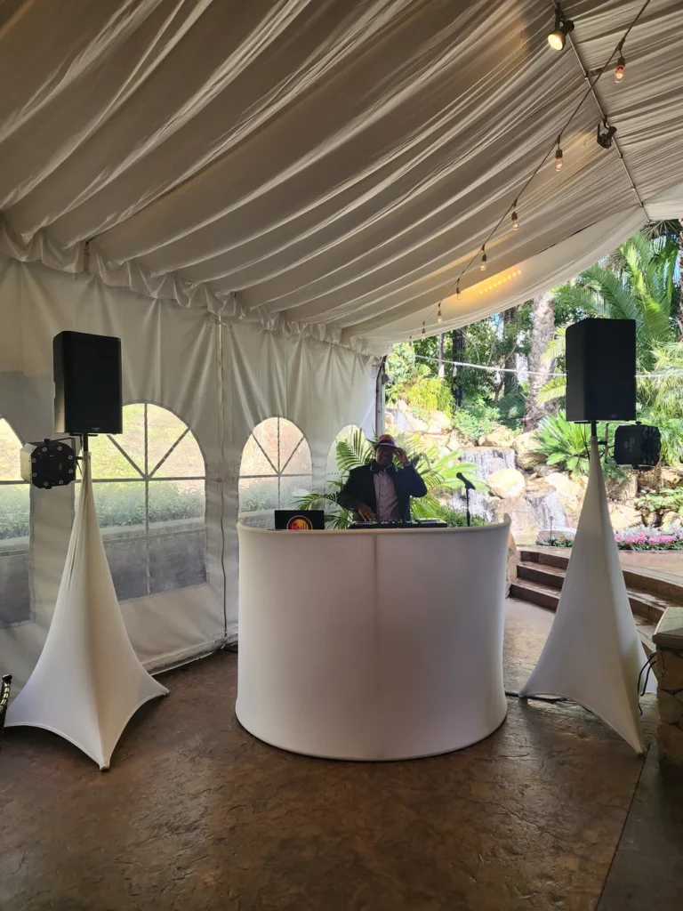 White DJ booth and coordinated speakers in a draped outdoor event tent.